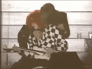 a man and a woman are hugging each other while playing a guitar in front of a window .