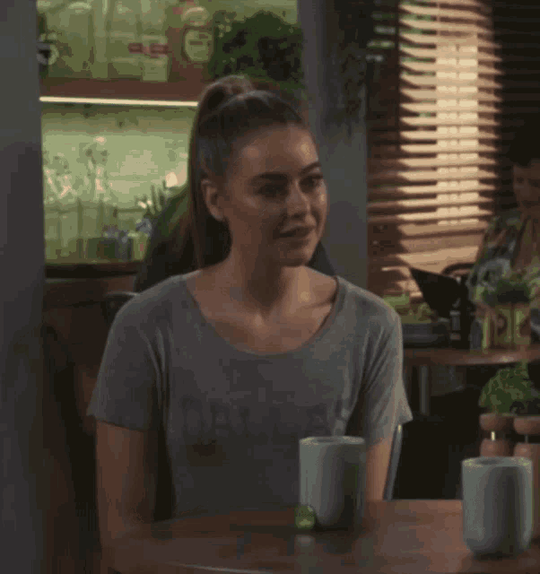 a woman wearing a grey shirt that says dallas sits at a table with two cups