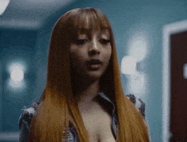 a woman with long red hair and bangs is standing in a hallway with a blue wall .