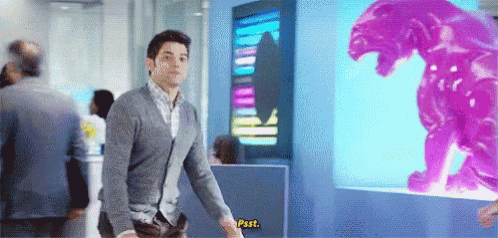 a man in a gray sweater is standing in front of a purple monster statue .