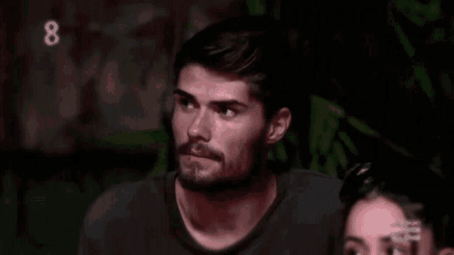 a man with a beard is looking at the camera with the number 8 behind him