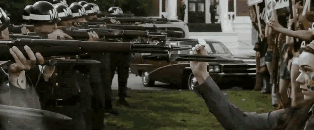 a man in a purple shirt is holding a gun in front of a row of police officers
