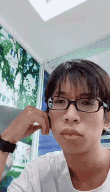 a young man wearing glasses and a white shirt is looking at the camera