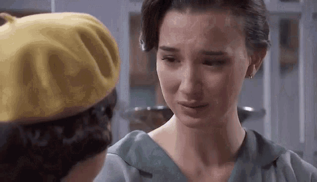 a woman in a yellow beret is crying next to another woman in a green dress .