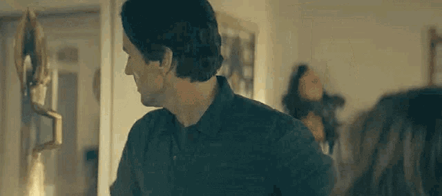 a man in a blue shirt is standing in a living room looking at a woman .
