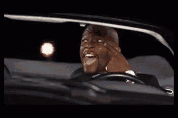 a man in a tuxedo is driving a black car at night .