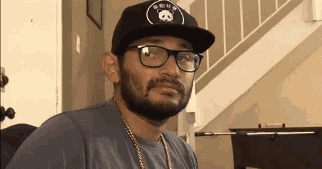 a man with a beard and glasses is wearing a hat and a chain .