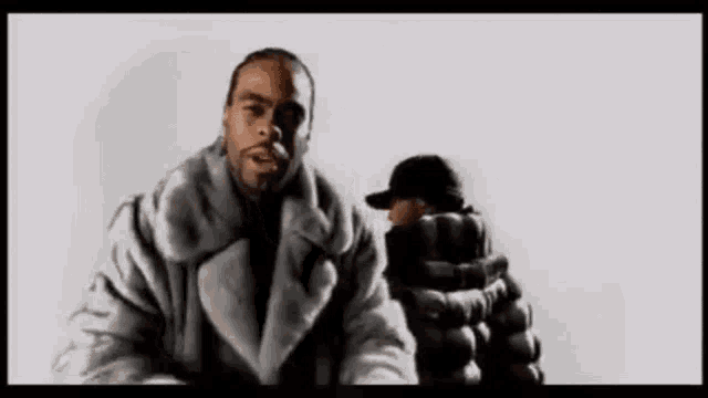 a man in a fur coat is standing next to another man in a black hat .