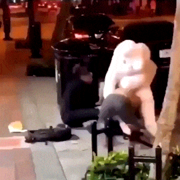 a person sitting on the sidewalk next to a black trash can