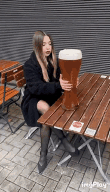 a woman is sitting at a table holding a large glass of beer