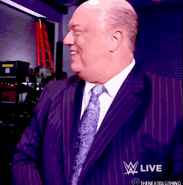 a bald man in a suit and tie is smiling in front of a sign that says ' w live '