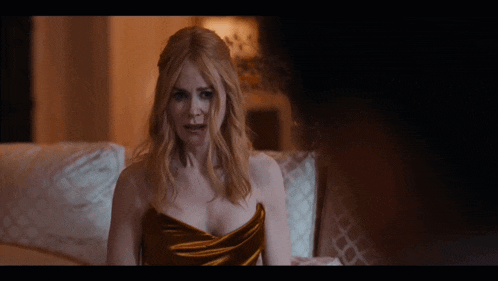 a woman in a gold dress sits on a bed