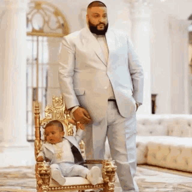 a man in a purple suit is standing next to a baby on a purple throne .