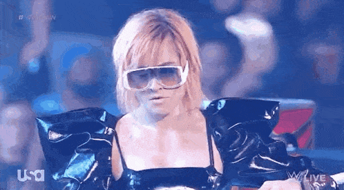 a woman wearing sunglasses and a leather jacket is standing in front of a crowd .