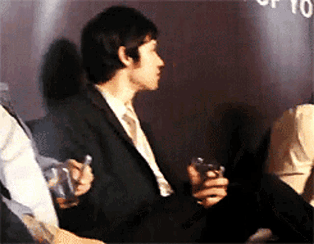 a man in a suit holds a glass in front of a sign that says ' a ' on it