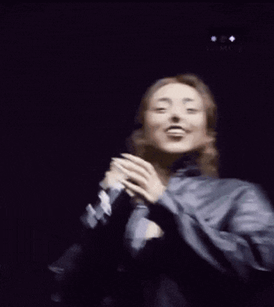 a woman is singing into a microphone while wearing a leather jacket and bra .