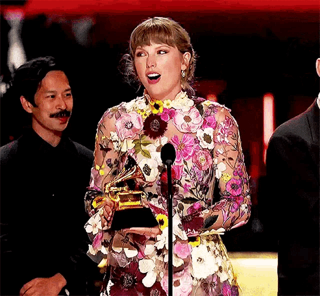 a woman in a floral dress is holding a trophy on a stage