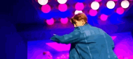a person in a blue jacket is dancing on a stage with pink lights behind them .