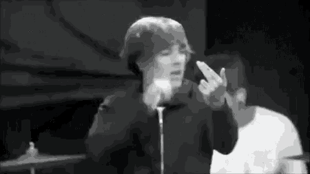 a black and white photo of a person singing into a microphone while giving the middle finger .