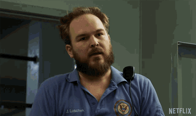 a man with a beard wears a blue shirt that says j. luschek