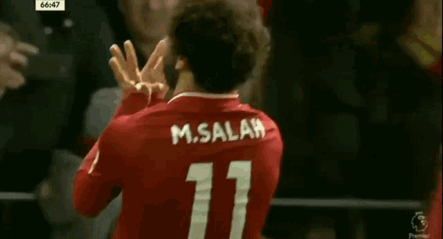 a soccer player wearing a red jersey with the number 11 on it is waving his hands in the air .