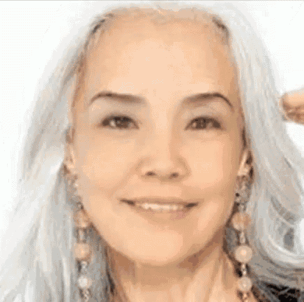 a close up of a woman with gray hair and earrings smiling .