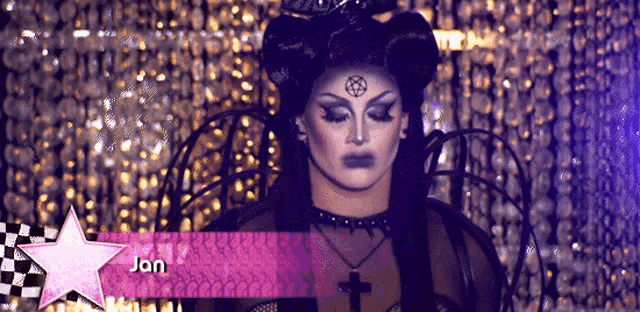 a drag queen with a cross on her forehead and the name jan on a pink star