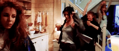 a group of women are dancing in a room with a pitcher of beer in the background .