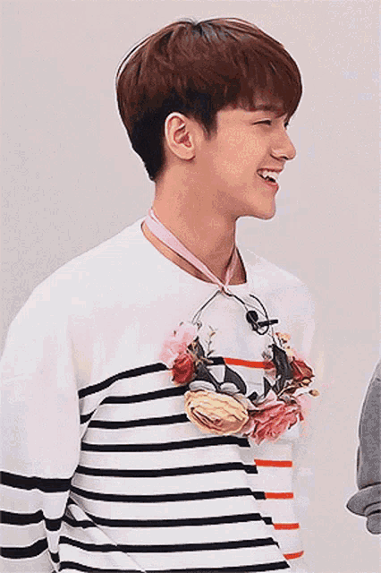 a young man wearing a striped shirt with flowers around his neck is smiling