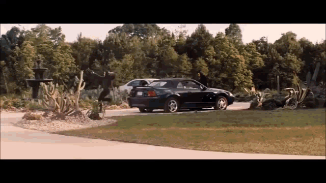 a black car is parked in a driveway in front of a fountain