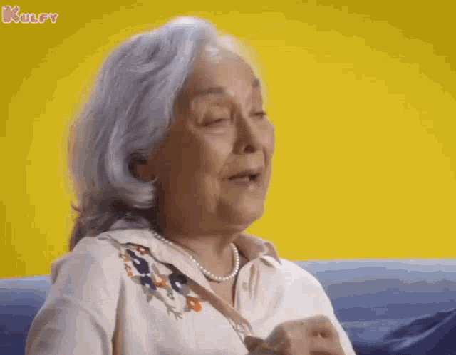 an elderly woman with gray hair is sitting on a blue couch with her eyes closed .