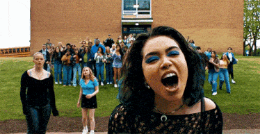 a girl with blue hair is screaming in front of a group of people .