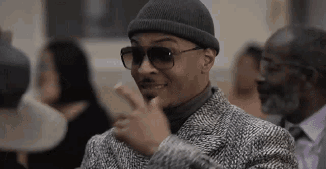 a man wearing sunglasses and a beanie is giving a thumbs up sign .