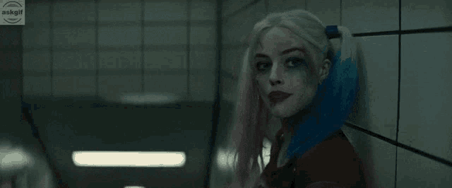 a woman in a harley quinn costume is standing in a hallway with the word huh written on the wall behind her