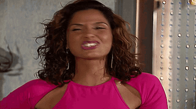 a woman with curly hair wearing a pink top and earrings