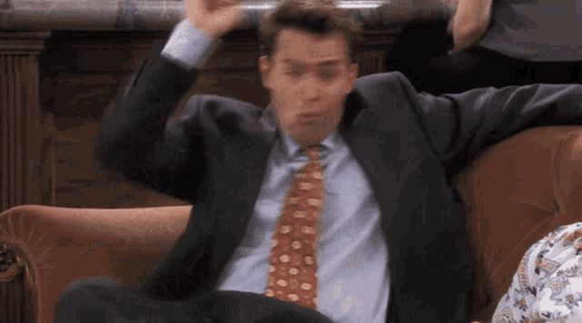 a man in a suit and tie sitting on a couch with his arms outstretched