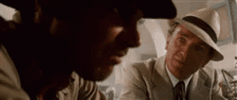 a man in a suit and hat is talking to another man in a hat .