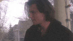 a man with long hair is sitting on a porch looking out the window