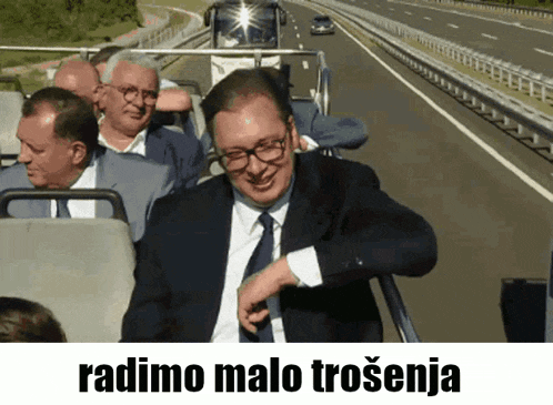 a man in a suit and tie is sitting on a bus with the words radimo malo trosenija written below him