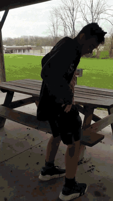 a man standing next to a wooden picnic table with his hands in his pocket
