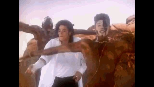 a man in a white shirt is standing next to a man in a mask in a desert .