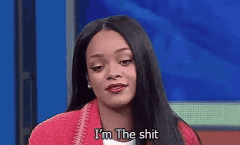 a woman is sitting in front of a blue wall and saying i 'm the shit .