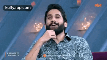 a man with a beard is sitting in a chair with his hand on his chin and smiling .