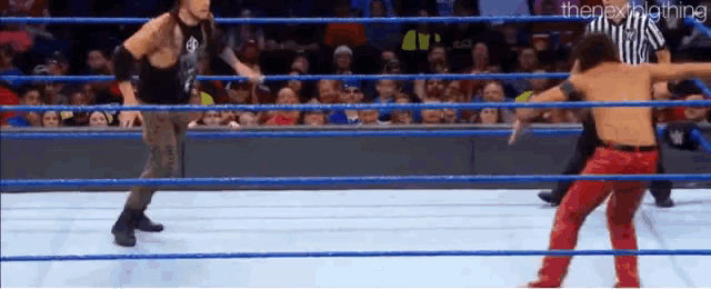 two wrestlers are fighting in a wrestling ring with a referee watching .