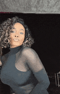 a woman with curly hair is wearing a black turtleneck sweater and gloves .