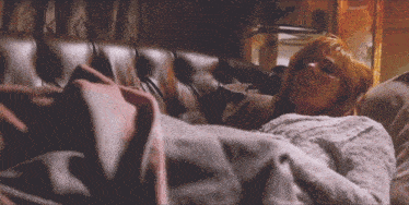 a woman with red hair is laying on a couch with a pink blanket