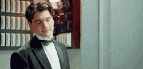 a man in a tuxedo and bow tie is standing in front of a wall .
