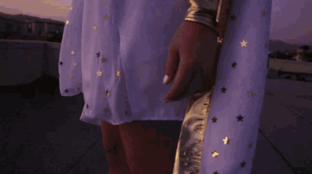 a woman wearing a white cape with gold stars on it looks out over a city