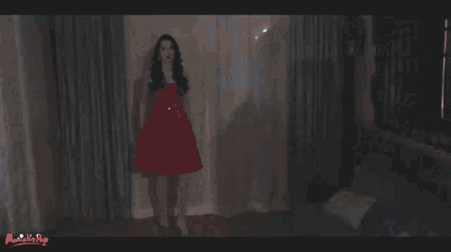 a woman in a red dress is dancing in front of a blue curtain that says music is hip