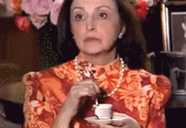 a woman in a red and orange dress is holding a cup of coffee and a saucer .